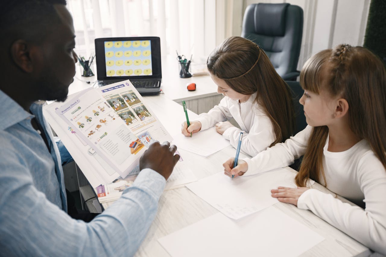 A teacher instructing two young students in a classroom environment.